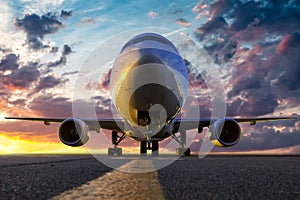 Front view of the wide body passenger jetliner at the airport apron against the backdrop of a scenic sunset sky