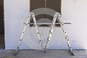 Front view of window frame, ladder and white concrete wall in incomplete house building site