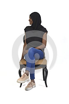 Front view of a woman with casual clothing and burka sitting on chair and looking at away and cross-legged