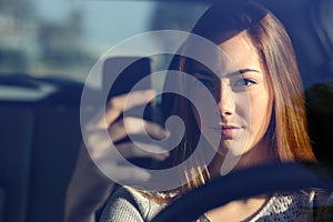 Front view of a woman driving a car and typing on a smart phone