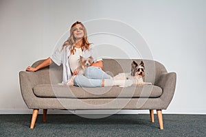 Front view. Woman is sitting on a sofa with two cute dogs