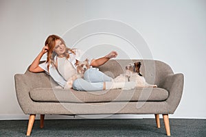 Front view. Woman is sitting on a sofa with two cute dogs