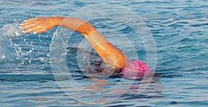 Front view of a women in a pink bathing cap swimming in a pool