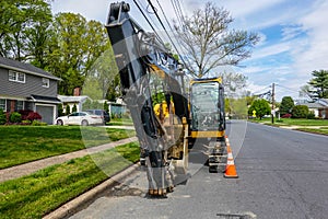 Front view of a yellow heavy equipment excavator parked on the side of a residential street in front of a house with orange