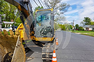 Front view of a yellow heavy equipment excavator parked on the side of a residential street in front of a house with orange