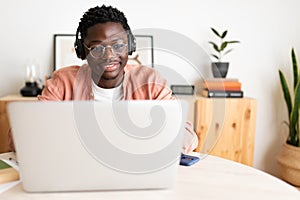 Front view of young African American man wearing headphones working, studying at home using laptop. Copy space.