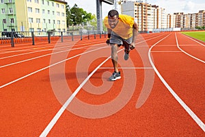 Front view of young afro american male sprinter in yellow sportswear running on the sport track. Concentrated tired