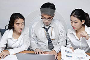 Front view of young Asian business people working together on a laptop computer at office. Teamwork brainstroming concept. Selecti