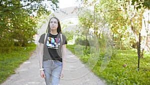 Front view of a young attractive walking girl with a backpack along the street. Medium shot.