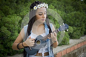 Front view of a young beautiful girl with braided hair, playing the ukulele