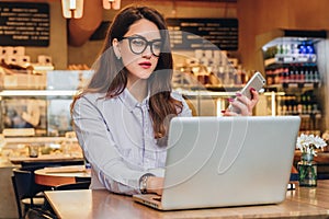 Front view. Young businesswoman is sitting in cafe working on laptop. Girl blogging, learning online, checking email.