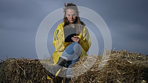 Front view young concentrated woman drawing in twilight sitting on haystack on field outdoors. Portrait of absorbed