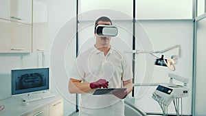 Front view of young dentist holding touchscreen, using virtual reality glasses. Male caucasian doctor working on