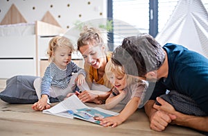 Young family with two small children indoors in bedroom reading a book.