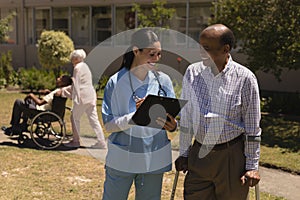 Front view of young female doctor discussing medical report with senior man on clipboard