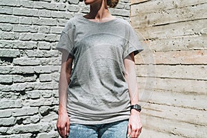 Front view. Young millennial woman dressed in gray t-shirt is stands against gray brick wall.