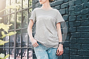 Front view. Young millennial woman dressed in gray t-shirt is stands against gray wood wall.