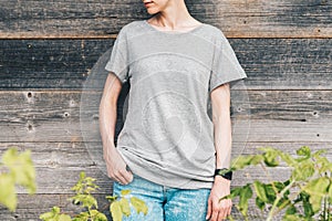 Front view. Young millennial woman dressed in gray t-shirt is stands against gray wood wall.