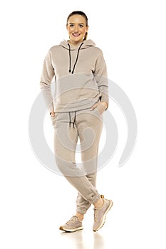 Front view of a young smiling woman in a gray tracksuit posing to a white background in the studio