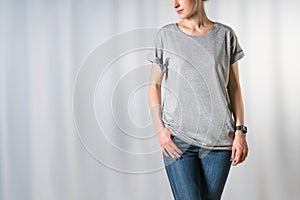 Front view of young woman, dressed in light gray t-shirt and blue jeans, standing on light gray background