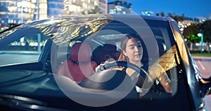 Front view of young woman driving car at night.