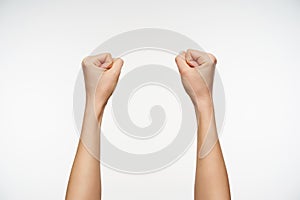 Front view of young woman`s hands being raised while clenching fingers into fists,  over white background. Body language