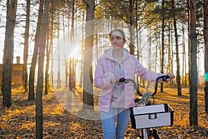 Young woman walking with bicycle in autumn city park - front view