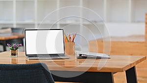 Front of white blank screen laptop, pencil holder, document files and potted plant .