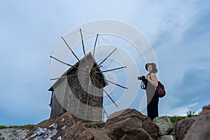 In front of the windmill, a teenage girl, a skilled photographer, captures the rustic charm.