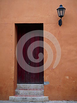 Front wooden door in  old town cartagena colombia  with a lamp on its side and orange wall