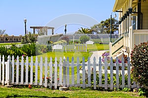 The front yard of the yellow lighthouse with a white picket fence. lush green grass and flowers with blue sky at Point Fermin Park