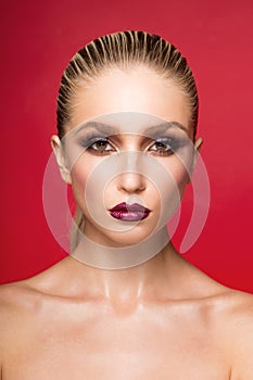 Frontal beauty portrait of young woman with perfect makeup with bare shoulders, over red background