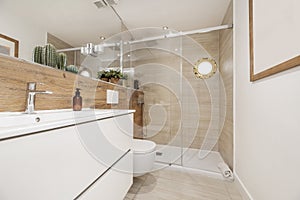 Frontal image of a bathroom with white furniture, tiled wall with wood-look tiles, infinity mirror and shower cabin with porthole