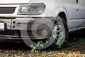 The frontal part of old van parked for years at parking lot with grass growing around. Wreck on a public road