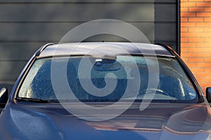 A frontal portrait of the frozen windshield of a car which is already almost melted so the driver can see again. The melted ice is