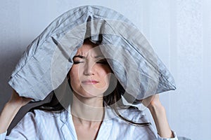 Frontal portrait of a lonely tired woman with a pillow on her head suffering from insomnia. Noisy neighbors, migraine, headache