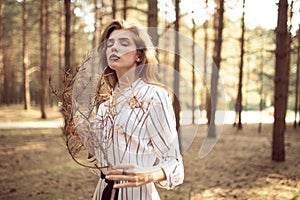 Frontal portrait of a outdoors fashion photo of beautiful young girl in the park with a pine branch in hands