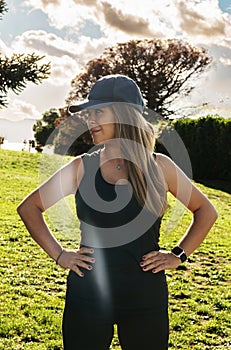 Frontal portrait of a young blonde-haired sporty woman in sportswear with her hands on her hips in a park