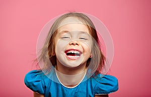 Frontal shot of laughter joyful little girl stands beside pink wall.