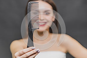 Frontal view of a beautiful young girl in a white razor. Combing hair. Close-up of a comb on a girl`s blurry background.