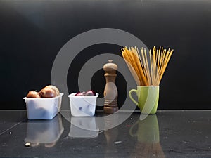 Frontal view, detail with two boxes with onion, a pepper and a green cup with spaghetti