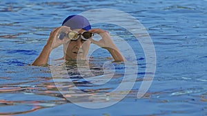 Frontal view of a professional swimmer in goggles by the pool. A female swimmer adjusts her glasses and starts a