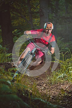 Frontal view of young caucasian male storming with a mountain bike over a berm on a singletrail. Epic ride with a modern mountain