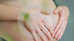 Frontal view of youthful beatiful women touches her tummy with child in garden interrior