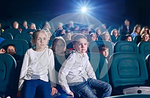 Frontview of little boy and girl sitting in the cinema hall.