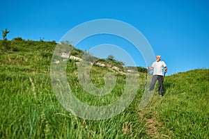 Frontview of old man walking on green field with tracking sticks.