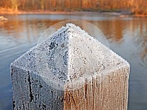 Frost covered wood pyramid post by lakeside in late Autumn