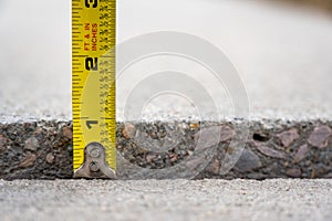 Frost heave crack in residential concrete sidewalk with tape measure