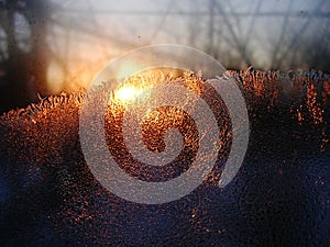 Frost ice crystals and water drops on window glass on the background of sunrise.