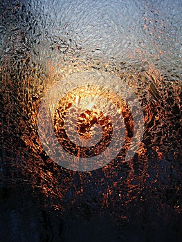 Frost ice crystals and water drops on window glass on the background of sunrise.